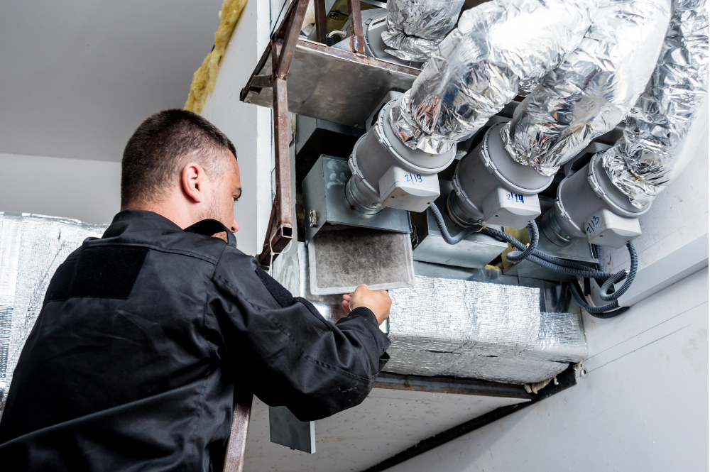 A technician replacing an indoor air filter unit as part of a custom mechanical ventilation system design setup by Pujnik.